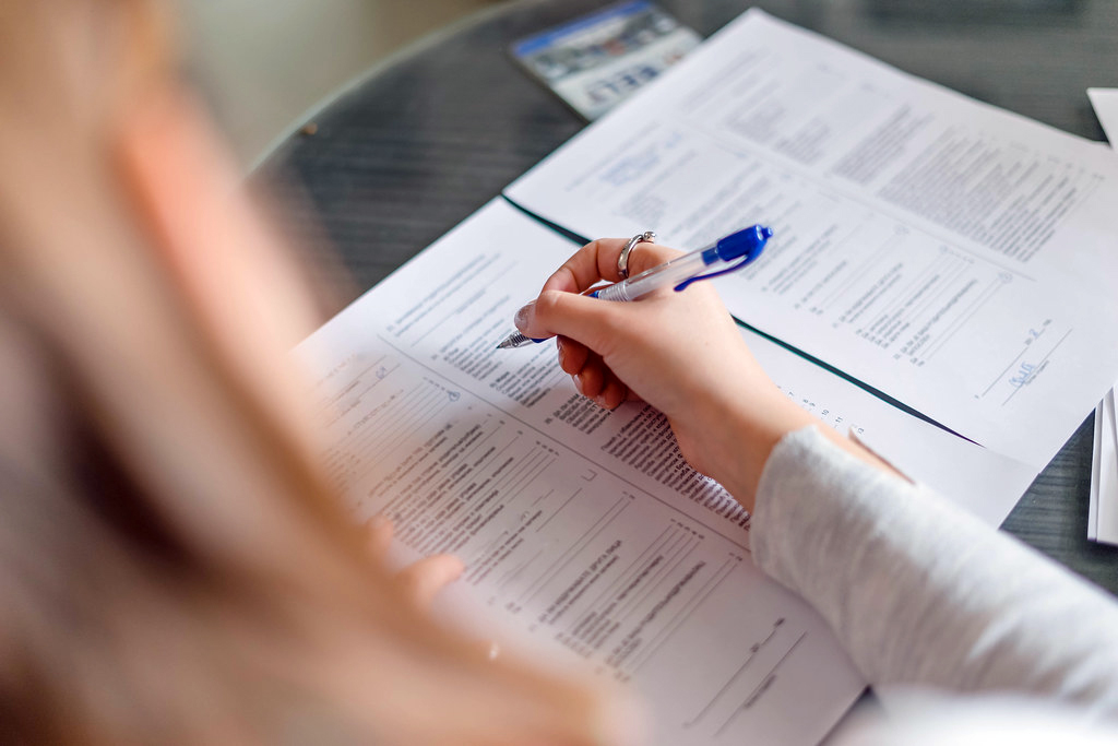 "Back View of Woman Filling Up The Papers in the Office" by Marco verch is licensed under CC BY 2.0